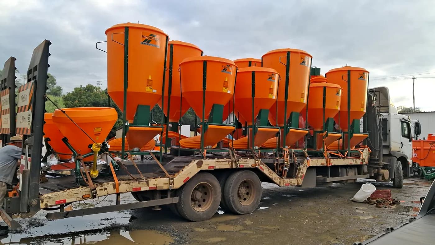 Caminhão prancha carregado com misturadores de ração e distribuidores Incomagri laranja, amarrados para o transporte.