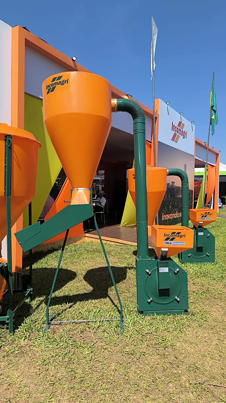 Misturadores de ração Incomagri laranja expostos na grama, em frente ao estande da fábrica.