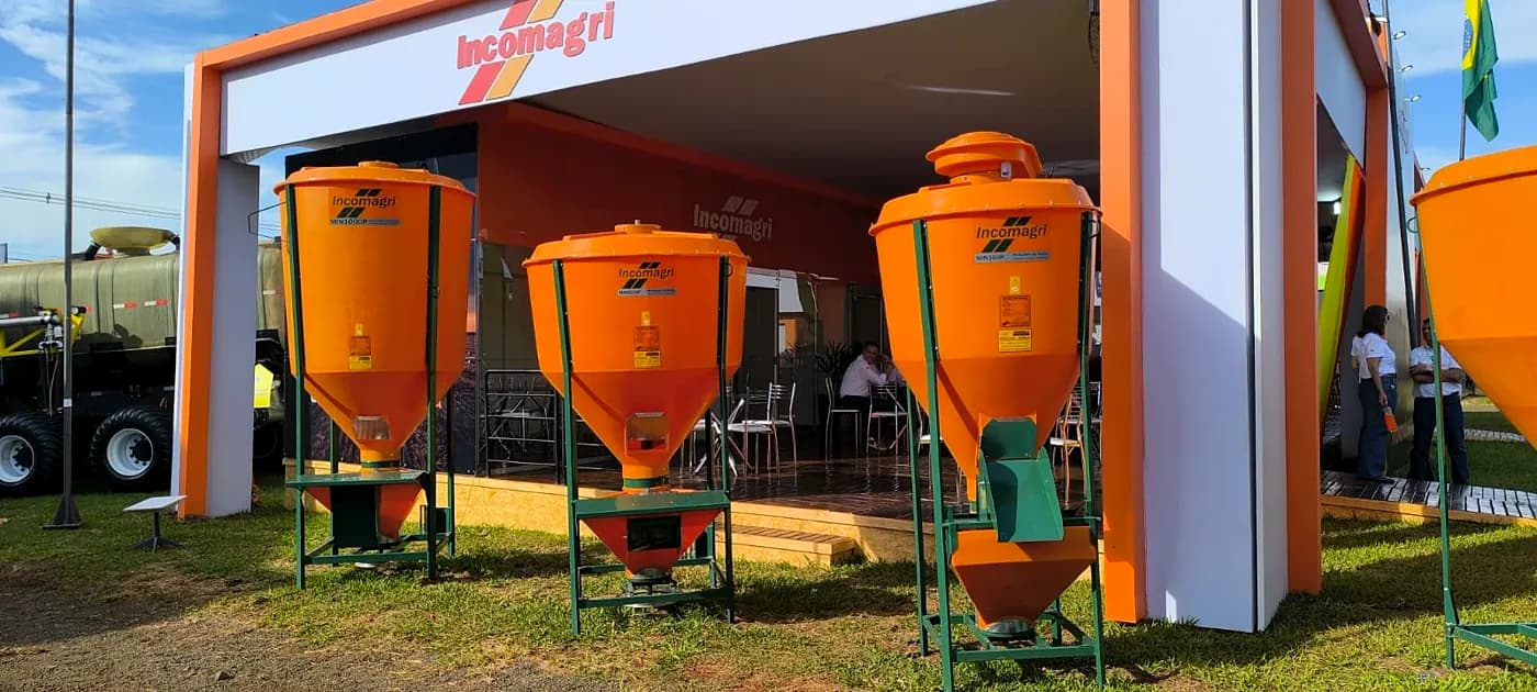 Fachada do estande da Incomagri em feira, com misturadores de ração laranja expostos na frente.