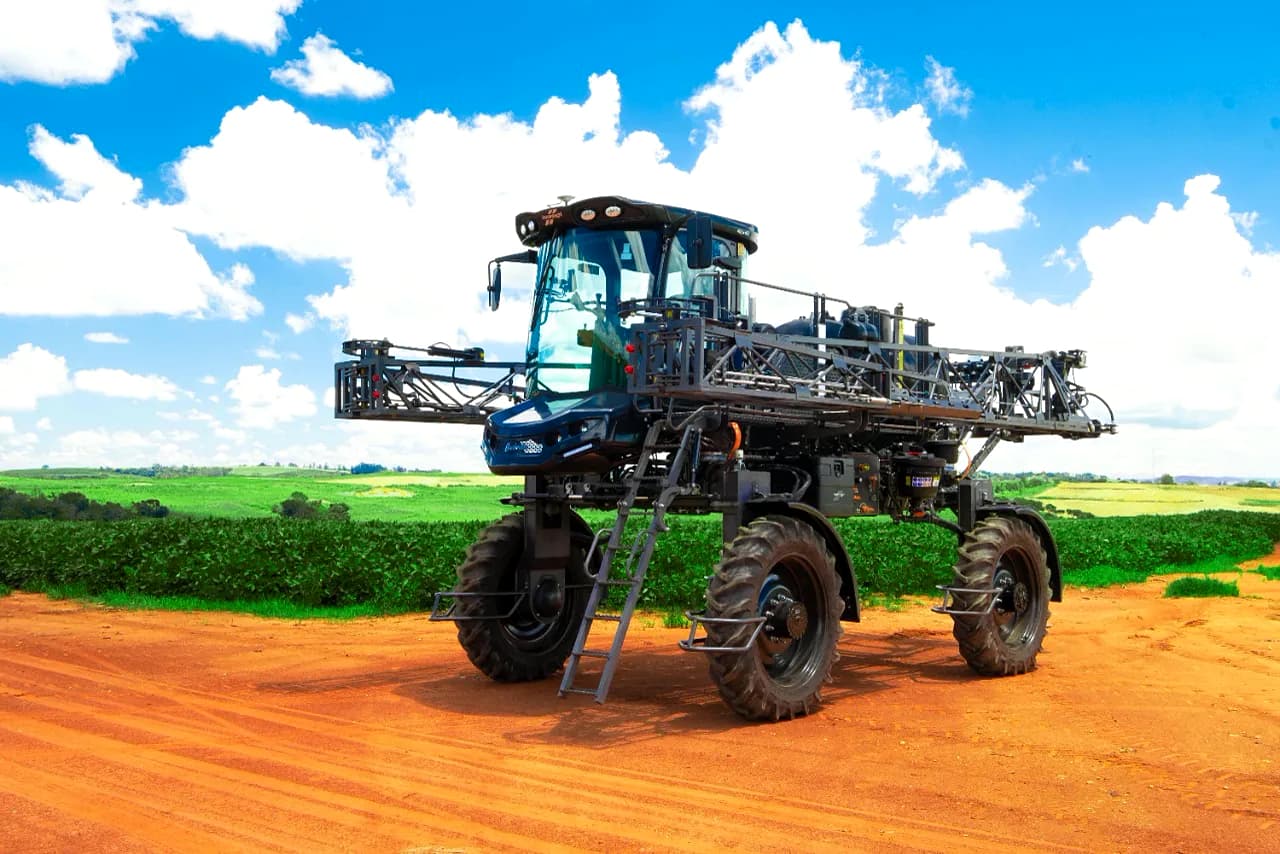 Pulverizador autopropelido Overlander com as barras recolhidas, parado em estrada de terra ao lado da lavoura.