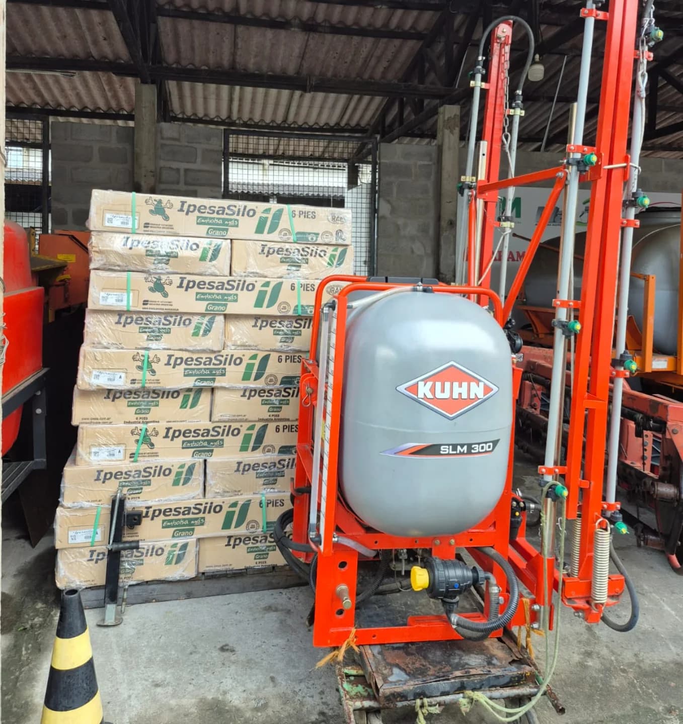 Estoque com caixas de bolsas Ipesa Silo de 6 pés ao lado de um pulverizador agrícola.